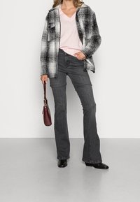 Sort og hvid ternet oversized skjortejakke over en lyserød v-hals sweater, kombineret med grå flare jeans og sorte ankelstøvler. Vinrød håndtaske.