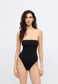 Μαύρο, στράπλες ολόσωμο μαγιό με ψηλή κοπή στο πόδι, λεία υφή και λεπτομέρειες σούρας μπροστά. Μινιμαλιστικός σχεδιασμός σε φωτεινό φόντο.