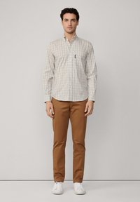 Camisa de cuadros en colores pastel con un bolsillo en el pecho, combinada con chinos marrones y zapatillas blancas. Tejido suave, corte ajustado.