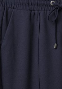 Mørkeblå joggebukser laget av mykt stoff, med elastisk midje, snøring i livet og sidelommer. Glatt tekstur uten synlige mønstre.