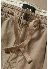 Pantalon en lin beige avec ceinture élastique, bouton marron et cordon de serrage assorti, montrant l'étiquette de la marque C&A à l'intérieur.