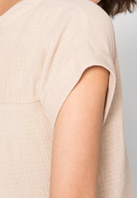 Top corto a maniche corte di colore beige chiaro realizzato in tessuto testurizzato, con una vestibilità comoda e maniche arrotolate. Design semplice e pulito senza motivi.
