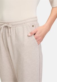 Lichtbeige joggers van een textuurstof, met een elastische tailleband, een trekkoord en zijzakken. Gouden accentdetails nabij de zak.