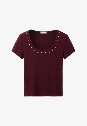 Bordové tričko s krátkym rukávom a okrúhlym výstrihom, zdobené dekoratívnymi striebornými cvočkami usporiadanými pozdĺž výstrihu pre zvýraznenie detailov.