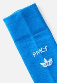 Blå bomullssokk med ribbestruktur, med hvite "RMCF"-bokstaver og et hvitt Adidas-logo på siden.