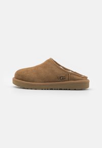 Zoccoli slip-on in camoscio marrone con rivestimento interno morbido, suola in gomma e dettagli di cucitura minimi. Logo UGG sul lato.