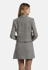 Zwart-wit houndstooth-gepatenteerde blazer met lange mouwen en een getailleerd ontwerp. Heeft een cropped lengte en geen zichtbare sluitingen.