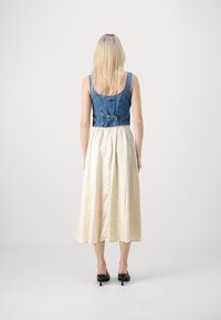 Denim avkortet topp med knappelukking på baksiden, kombinert med en flytende, ankellang kremfarget skjørt med en teksturert overflate. Svarte hæler.