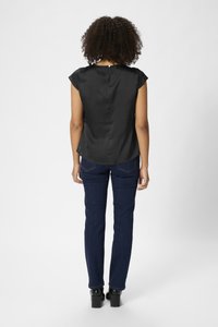 Haut en satin noir avec des manches courtes, détail en clé à l'arrière, porté avec un jean fitted bleu foncé et des bottes à talons chunky noires.