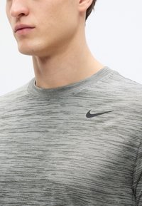 Γκρι αθλητική μπλούζα με ανάγλυφη υφή, στρογγυλή λαιμόκοψη, κοντά μανίκια και μικρό μαύρο λογότυπο Nike στο στήθος.