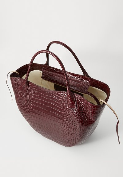 Τσάντα τσάντα σε μπορντό από δέρμα κροκοδείλου με δύο στρογγυλές λαβές, ανοιχτή κορυφή και εσωτερική τσέπη με φερμουάρ. Απαλή εσωτερική επένδυση.