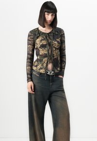 Langsleeve top in camouflage- en bloemenprint stof, met een strik aan de voorkant; gecombineerd met wijde, vervaagde jeans met een ceintuursluiting.