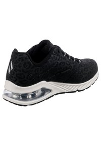 Chaussure de sport noire avec un motif léopard subtil, semelle intermédiaire blanche, coussin d'air transparent au talon et lacets noirs et blancs inclinés pour montrer le côté extérieur.
