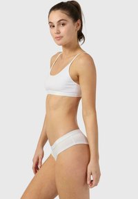Balti bralete un hipster apakšveļu komplekts, kura izceļas ar gludu tekstūru un vieglu spīdumu uz jostas. Minimalistisks dizains, pieguļošs siluets.