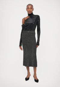 Černý top na jedno rameno s flitry, zkombinovaný s dlouhou, přiléhavou, hřebenovou černou sukní. Elegantní textura a třpytivé detaily po celém povrchu.