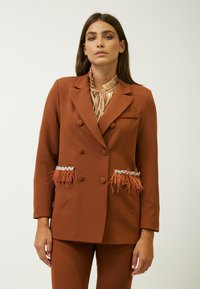 Blazer marrone doppiopetto con accenti di piume e tasche decorate. Tessuto liscio, vestibilità su misura e maniche lunghe.