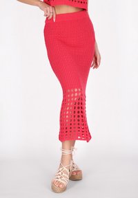 Roze gebreide rok met een ribbelpatroon, voorzien van uitsnijdingen nabij de zoom en een aansluitende tailleband. Gecombineerd met lichtgekleurde wedges.