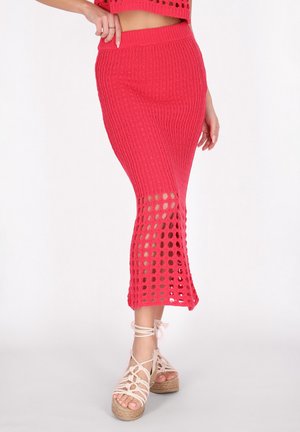 Roze gebreide rok met een ribbelpatroon, voorzien van uitsnijdingen nabij de zoom en een aansluitende tailleband. Gecombineerd met lichtgekleurde wedges.