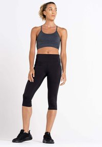 Sport-BH in Dunkelgrau mit Mesh-Akzenten, kombiniert mit schwarzen Capri-Leggings. Das Model trägt schwarze Sportschuhe und steht vor einem weißen Hintergrund.