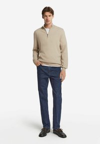 Beige kvartdraget tröja, mjukt stickat tyg, avslappnad passform. Kombinerad med mörka denimjeans och bruna skor med snördetaljer.