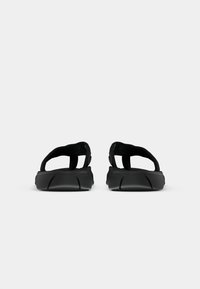 Sandalias negras con un diseño elegante, que presentan tiras anchas y una suela texturizada. El material es similar al caucho con un acabado suave.