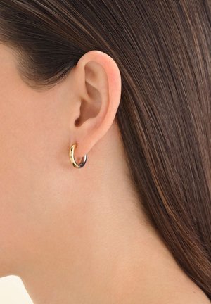 Boucle d'oreille en or et argent présentée sur l'oreille d'une personne, avec une finition métallique lisse et un design simple et arrondi.