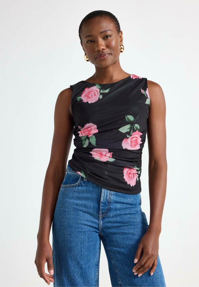 Sort ærmeløs top med pink rosemønster, der har et draperet design. Sammen med højtaljede blå denim jeans, hvilket fremhæver et afslappet look.