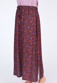 Langer Blumrock mit einem lila Grundton und roten sowie lila Blumenmustern, einem elastischen Bund und einem seitlichen Schlitz für bessere Bewegungsfreiheit.