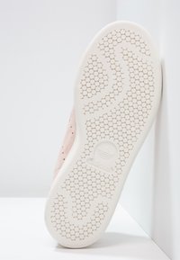 Vitt gummisul av Adidas-sko med cirkulärt mönster och Adidas-logotyp centrerad på en ljusrosa mockaöverdel.