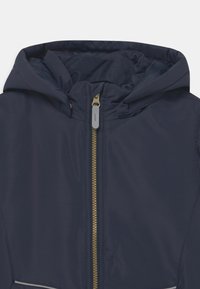 Veste bleu marine avec capuche, fermeture éclair centrale dorée et tirette réfléchissante sur la fermeture éclair.