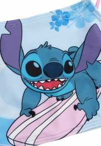 Blauter Stoff mit einem Cartoon-Charakter, der große Ohren, ein breites Grinsen und ein pinkes Surfbrett hat, akzentuiert mit blauen Blumenmustern.