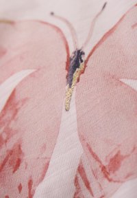 Blommönstrad tyg med en rosa fjärilsdesign och guldiga detaljer, mjuk textur och en detaljerad illustration på en ljus bakgrund.