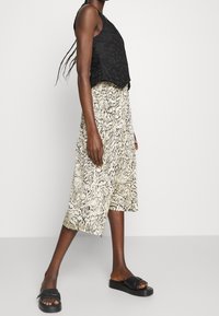 Sort crop top med tekstureret stof, kombineret med en løs knælængde nederdel med abstrakt mønster i sort og creme. Sorte slid-sandaler.