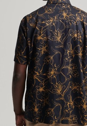 Laivastonsininen lyhythihainen paita, jossa on kultainen kukkakuviointi, yllään henkilö, joka näkyy selkäpuolelta ja jonka käsivarsi on näkyvissä.