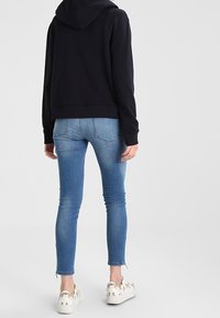 Felpa nera con cappuccio, lunghezza media; jeans skinny azzurri con leggero strappo alle caviglie; sneakers bianche con dettagli dorati e motivi animali.