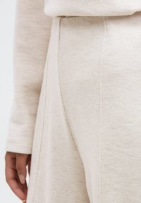 Beige sweatpants feature a soft, textured fabric with visible stitching along the seams. A hand rests gently on the fabric's surface.