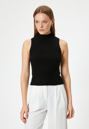 Zwarte mouwloze gebreide top met een hoge halslijn, met een ribbelstructuur en een aansluitende pasvorm, gecombineerd met witte broek.