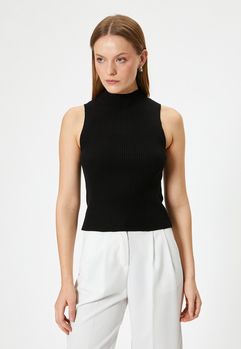 Zwarte mouwloze gebreide top met een hoge halslijn, met een ribbelstructuur en een aansluitende pasvorm, gecombineerd met witte broek.