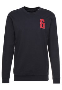 Granatowa bawełniana bluza z długimi rękawami, ribbed crew neck oraz czerwonym haftowanym logo „&” na lewej piersi. Gładka tekstura.