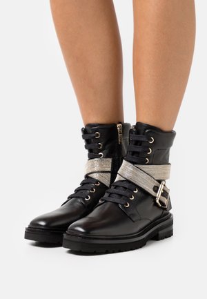 Bottes en cuir noir à la cheville avec semelles épaisses, lacets noirs, fermetures éclair latérales et larges bandes argentées pailletées avec boucles autour des chevilles.