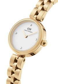 Montre dorée avec un cadran rond blanc, marqué par quatre marqueurs d'heure en accent diamant et un bracelet à maillons poli. Logo de la marque visible.