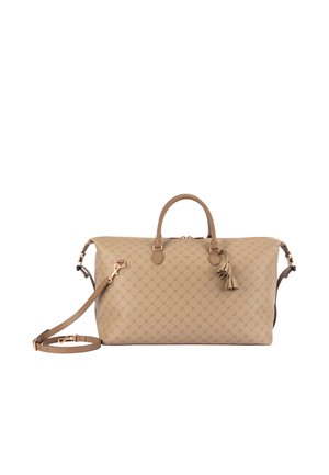 Sac polochon beige à motifs avec deux poignées, une bandoulière amovible et un pompon décoratif suspendu près de la fermeture éclair.