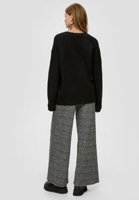 Schwarzer Pullover mit weitem Halsausschnitt und gerippten Bündchen, kombiniert mit hoch taillierten, grau gestreiften weit geschnittenen Hosen und schwarzen Plateauschuhen.