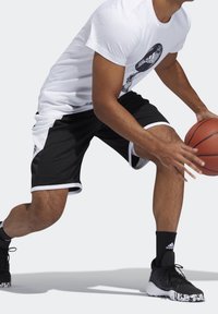 Schwarz-weiße Sportshorts mit seitlichen Mesh-Einsätzen, kombiniert mit einem weißen T-Shirt mit schwarzem Logo und schwarzen Basketballschuhen.