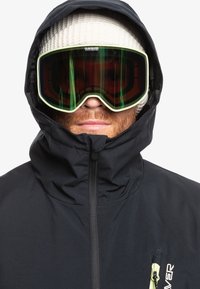 Schwarze isolierte Jacke mit hohem Kragen, Reißverschlussverschluss und einer linken Brusttasche. Getragen mit einer weißen Strickmütze und einer Skibrille.