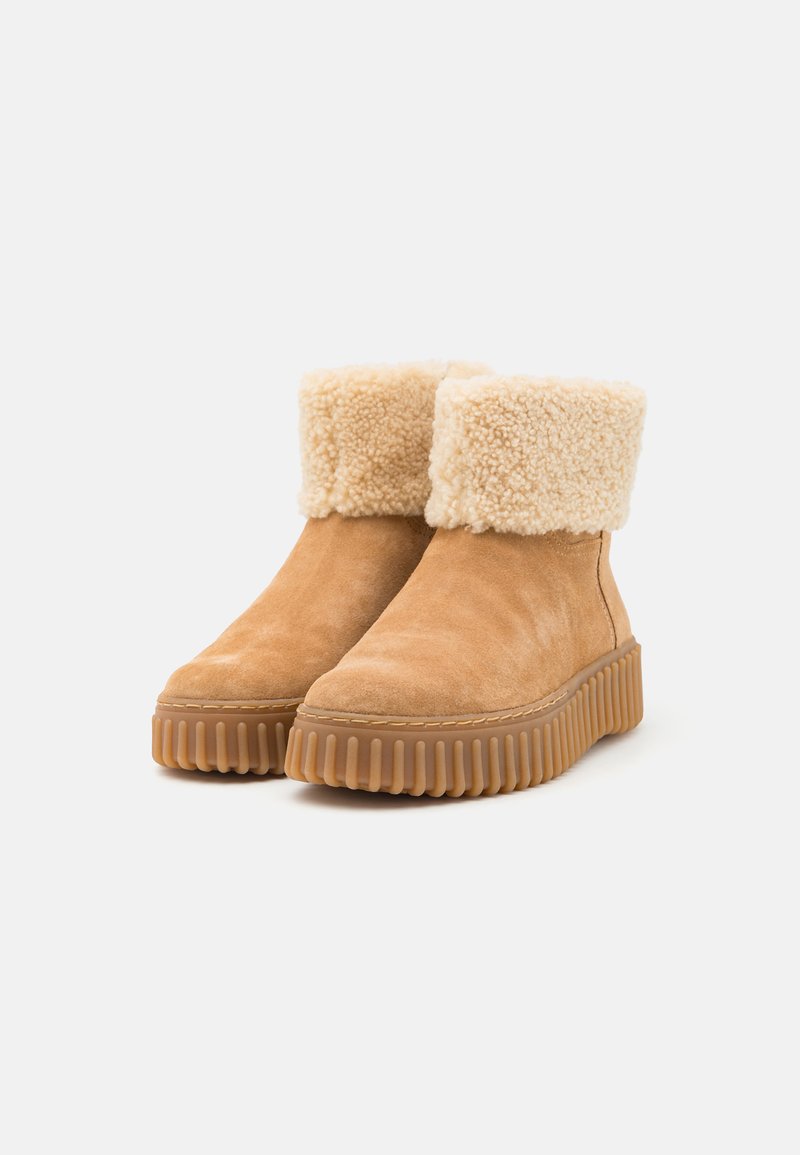 Bottines en daim tan avec un col en fausse fourrure beige texturée, semelle en caoutchouc robuste avec des rainures, et des coutures le long du bord.