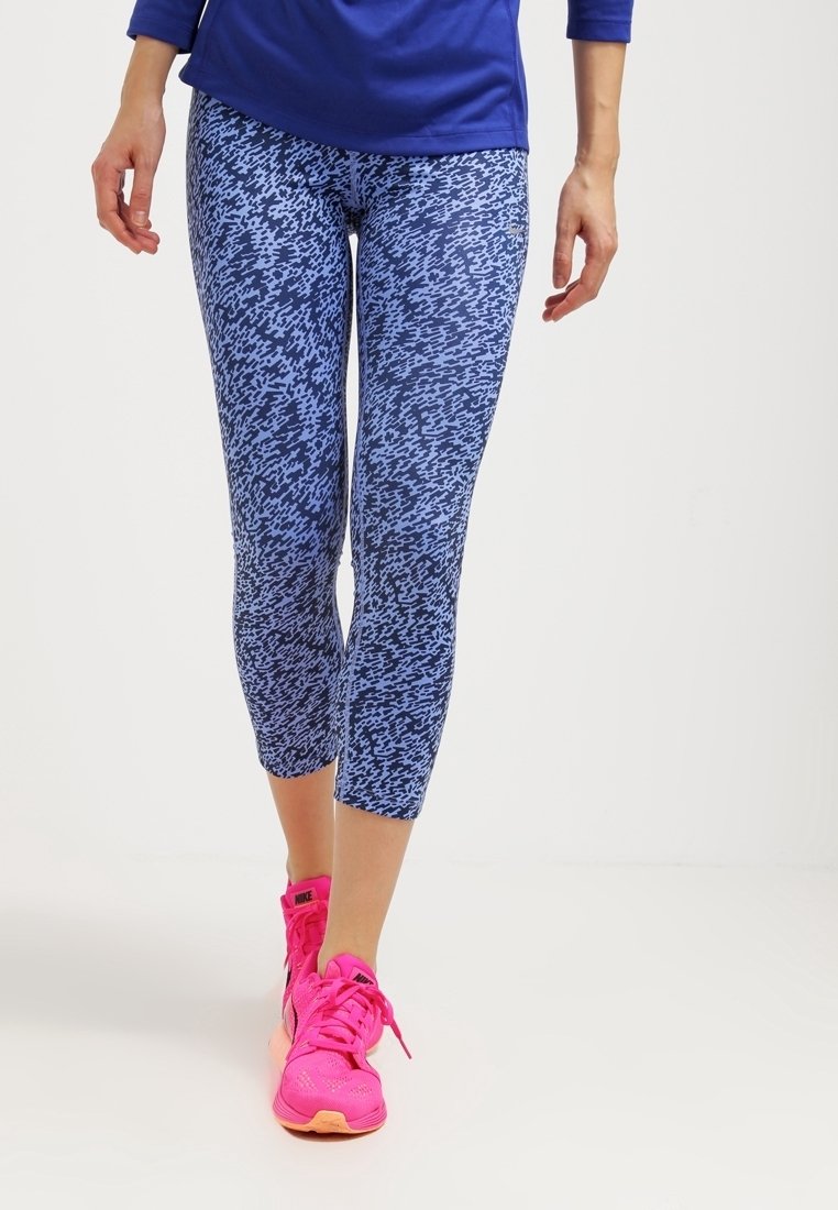 Niebieskie legginsy w wzory z teksturowanym designem, o długości do połowy łydki, połączone z jasnoróżowymi butami sportowymi.
