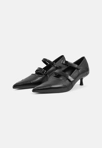 Chaussures en cuir noir avec des pointes effilées et un petit talon. Présentent deux sangles décoratives sur le dessus et des détails de couture subtils.