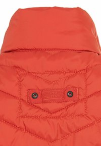 Czerwony kołnierz pikowanej kurtki z metką i dwoma czarnymi metalowymi zatrzaskami. Ozdobiony wzorem pikowania w kszta�łcie diamentu. Gładka, syntetyczna tekstura tkaniny.