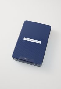 Scatola di latta blu navy con una finitura liscia, dotata di un'etichetta bianca che riporta la scritta "TOMMY HILFIGER" e le specifiche di taglia per calzini normali.